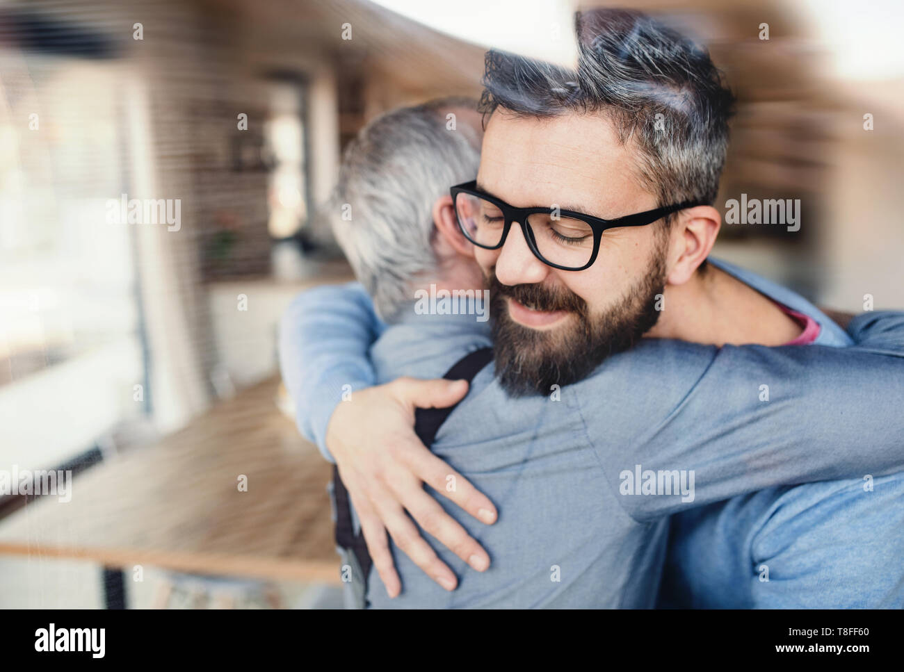 Ein erwachsener hipster Sohn und Vater in Innenräumen zu Hause, umarmen sich. Stockfoto