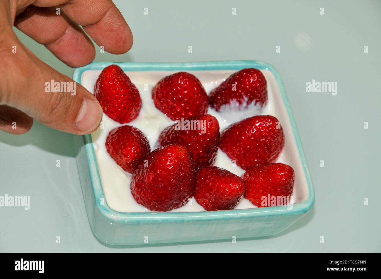 Eine Hand wird durch eine Schale mit frischen Erdbeeren und Sahne gesunden Snack versucht Stockfoto
