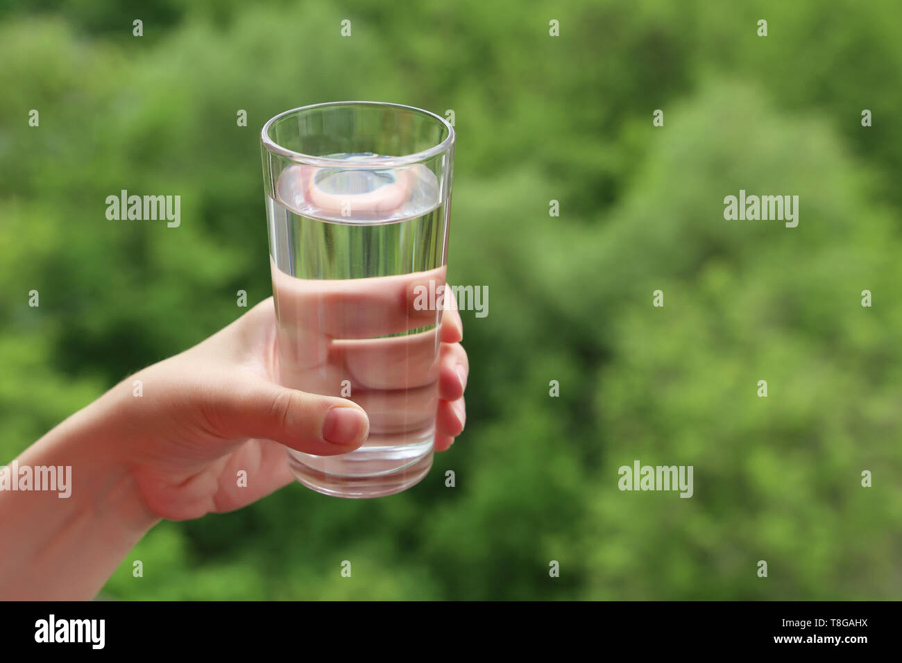Glas sauberes Trinkwasser in weiblicher Hand auf unscharfen Natur Hintergrund. Konzept der Durst, Wasseraufbereitung und Ökologie, gesunde Ernährung Stockfoto