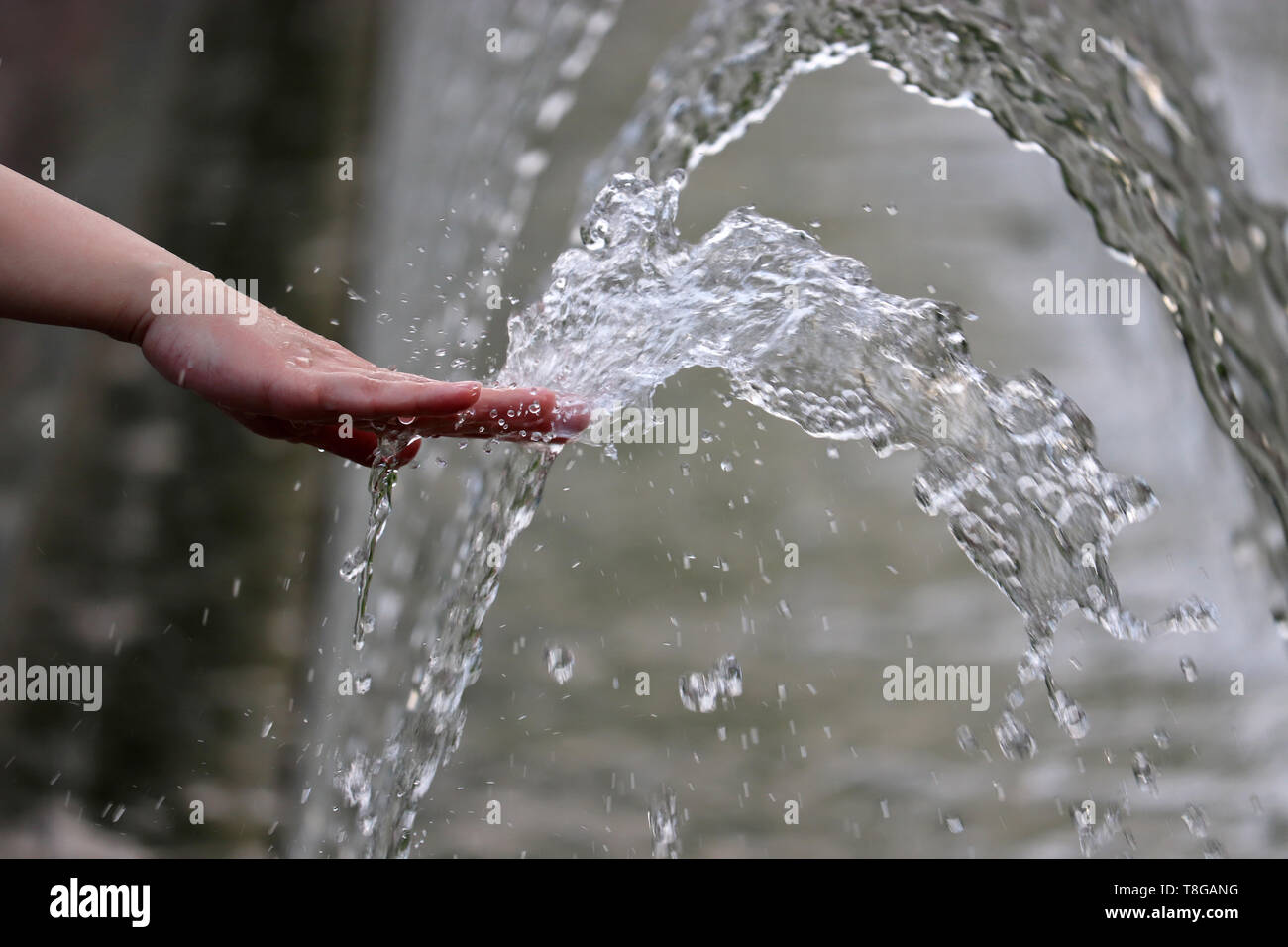 Frische und Kühle, weibliche Hand in einem Wasser des Brunnens. Mädchen spielen mit Spritzenden Düsen, Konzept der Feuchte, heisse Sommer Wetter Stockfoto