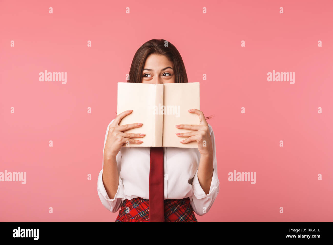 Portrait von Schulmädchen 15-16 y in Schuluniform lesen Buch beim Stehen über den roten Hintergrund isoliert Stockfoto