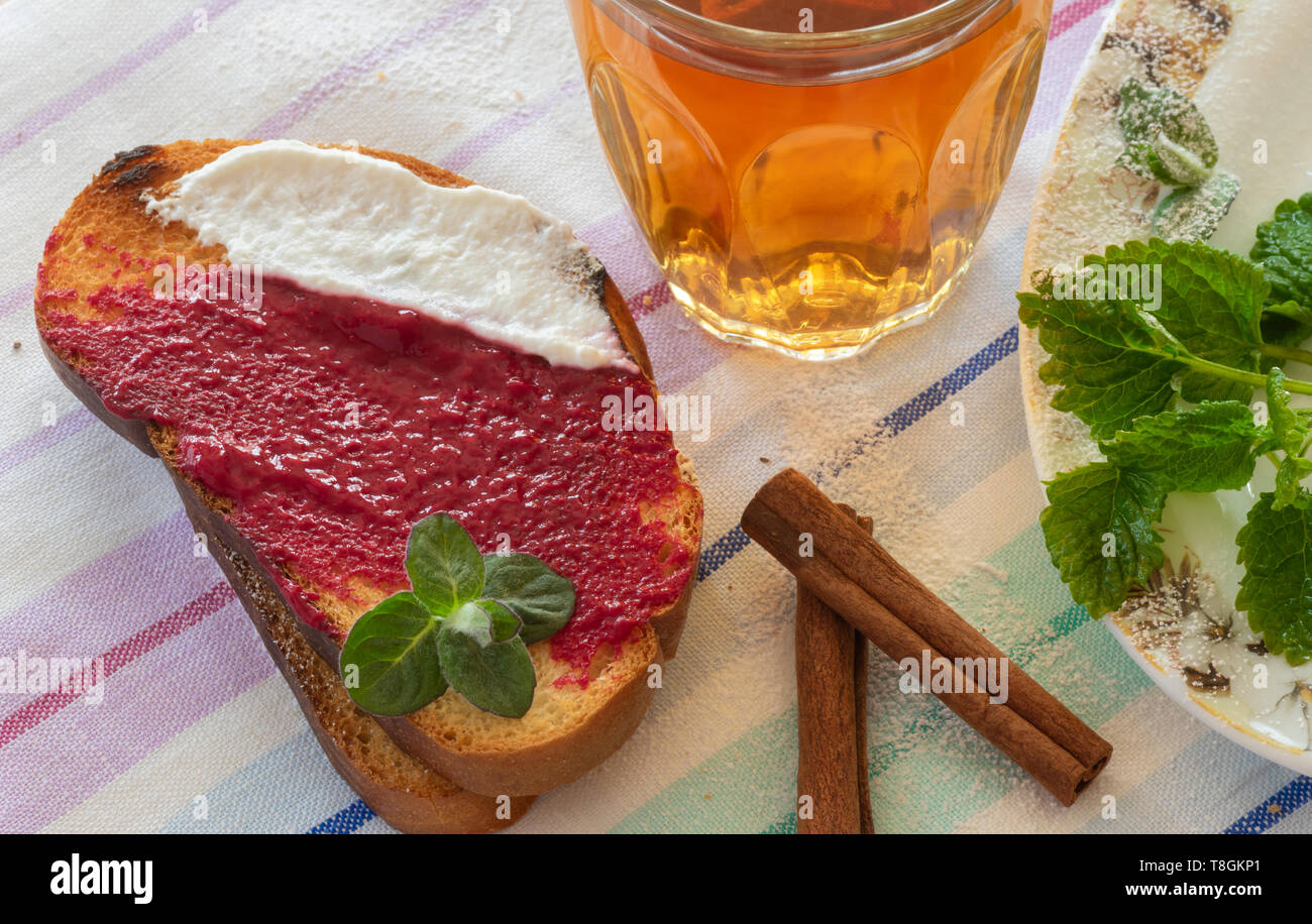 Zwei Toast mit Himbeere Maische und Joghurt, Glas Tee, Zimt und Minze. Stockfoto