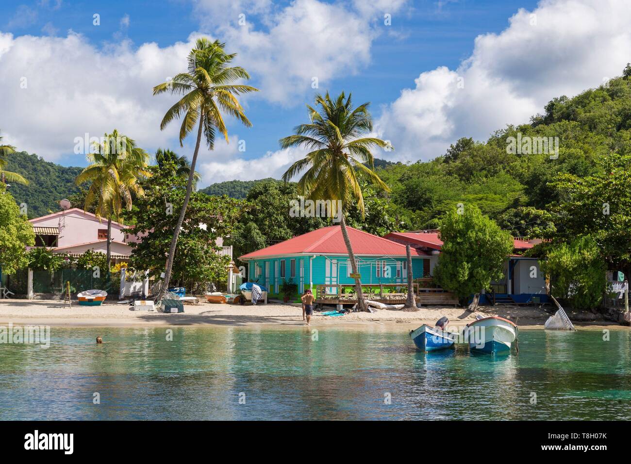 Martinique, am Strand von Anses d'Arlets, Häuser am Rande des Wassers und badegast im Vordergrund Fischerboote vor Anker am Strand Boote Stockfoto