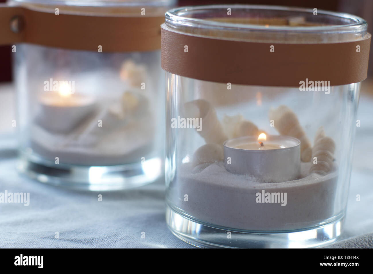Zwei Gläser mit brennenden Kerzen auf dem Tisch, leicht blau Gamma Stockfoto