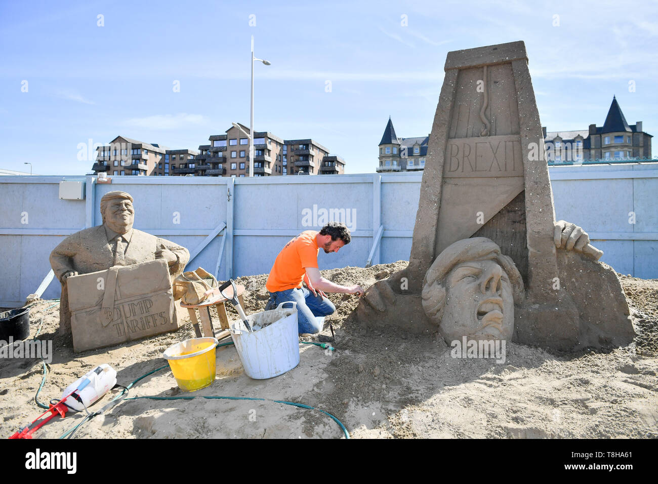 Sand Skulptur Künstler Johannes Hogebrink arbeitet an einem Brexit themed Skulptur an der Weston Sandskulpturenfestival, Weston-super-Mare. Die Skulptur mit Premierminister Theresa kann ihren eigenen Kopf weg schneiden mit einer Guillotine während US-Präsident Donald Trump Uhren auf. Stockfoto