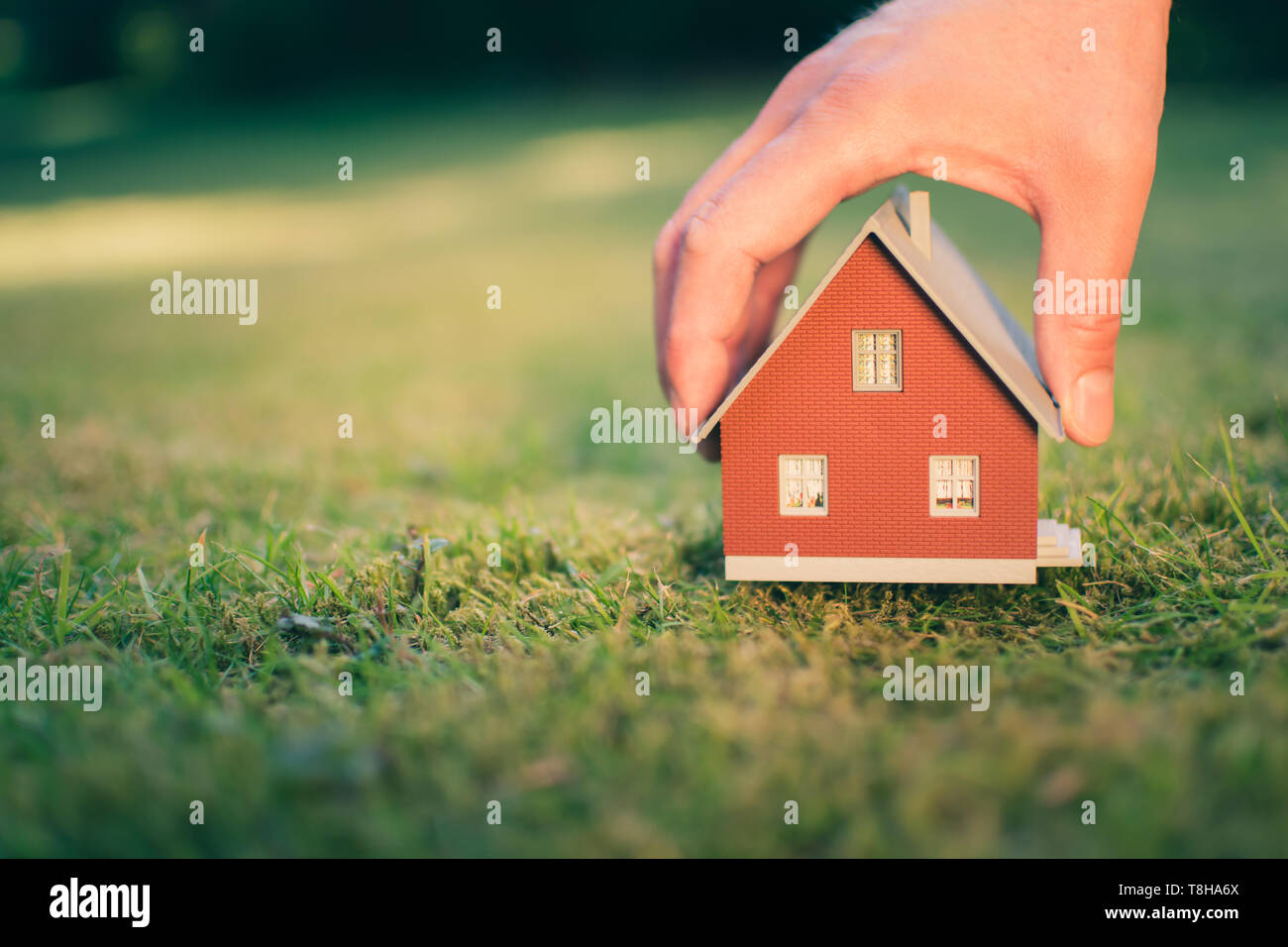 Konzept der Verkauf eines Hauses. Eine Hand hält ein Modell Haus oberhalb der grünen Wiese. Stockfoto