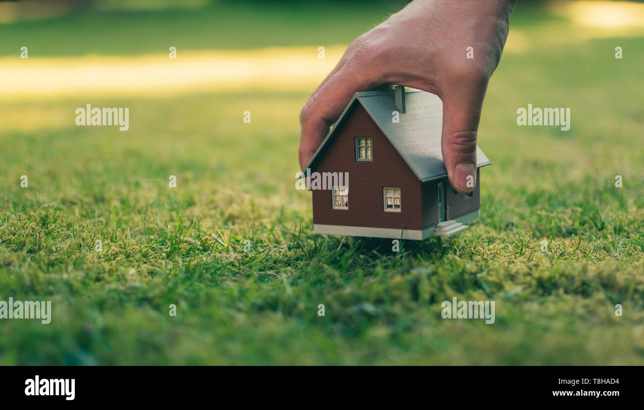 Konzept der Verkauf eines Hauses. Eine Hand hält ein Modell Haus oberhalb der grünen Wiese. Stockfoto