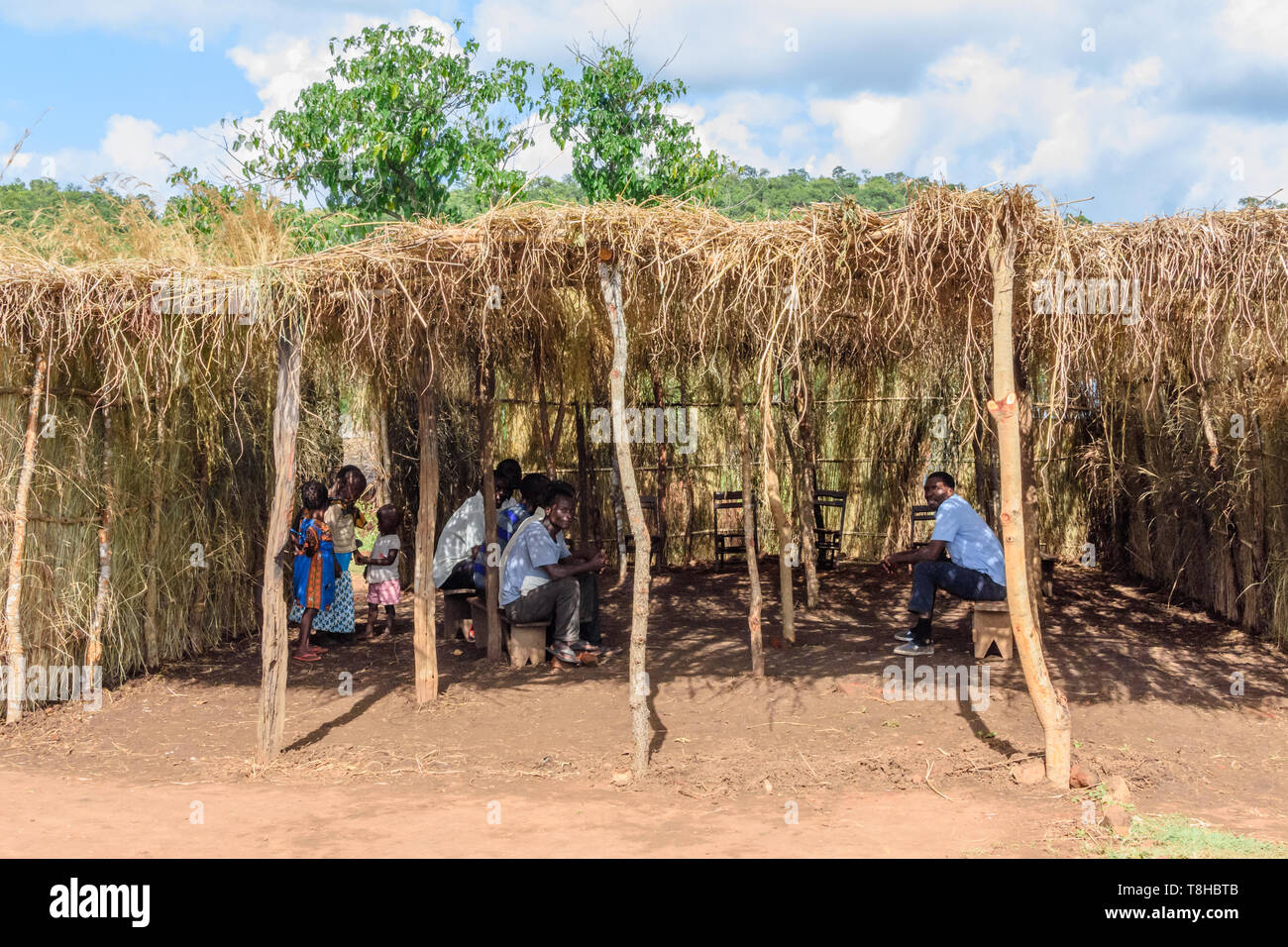 Malawische Männer sitzen auf Holzbänken unter einem Gras Tierheim zusammen zu beten. Stockfoto