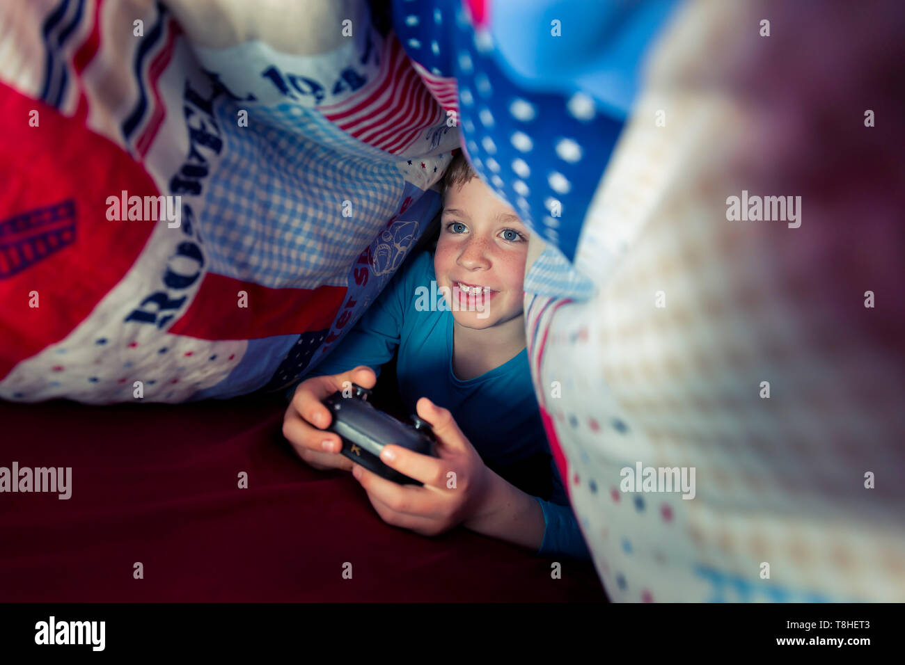 Junge, 8 Jahre, sectretly spielen, computer spiel im Bett Stockfoto