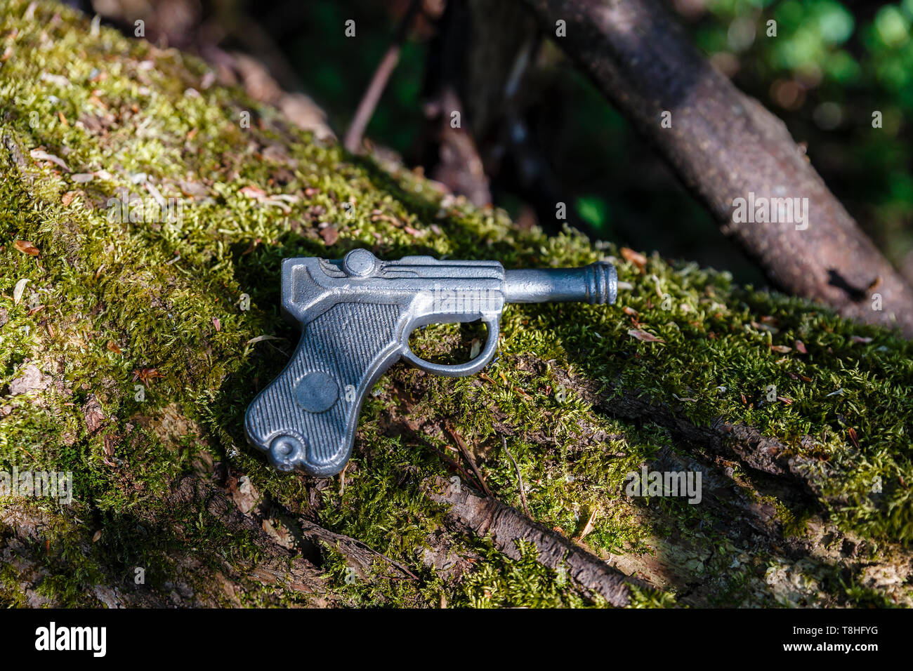 Spielzeugpistole aus Blei liegt auf einem alten Baum mit Moos. Stockfoto