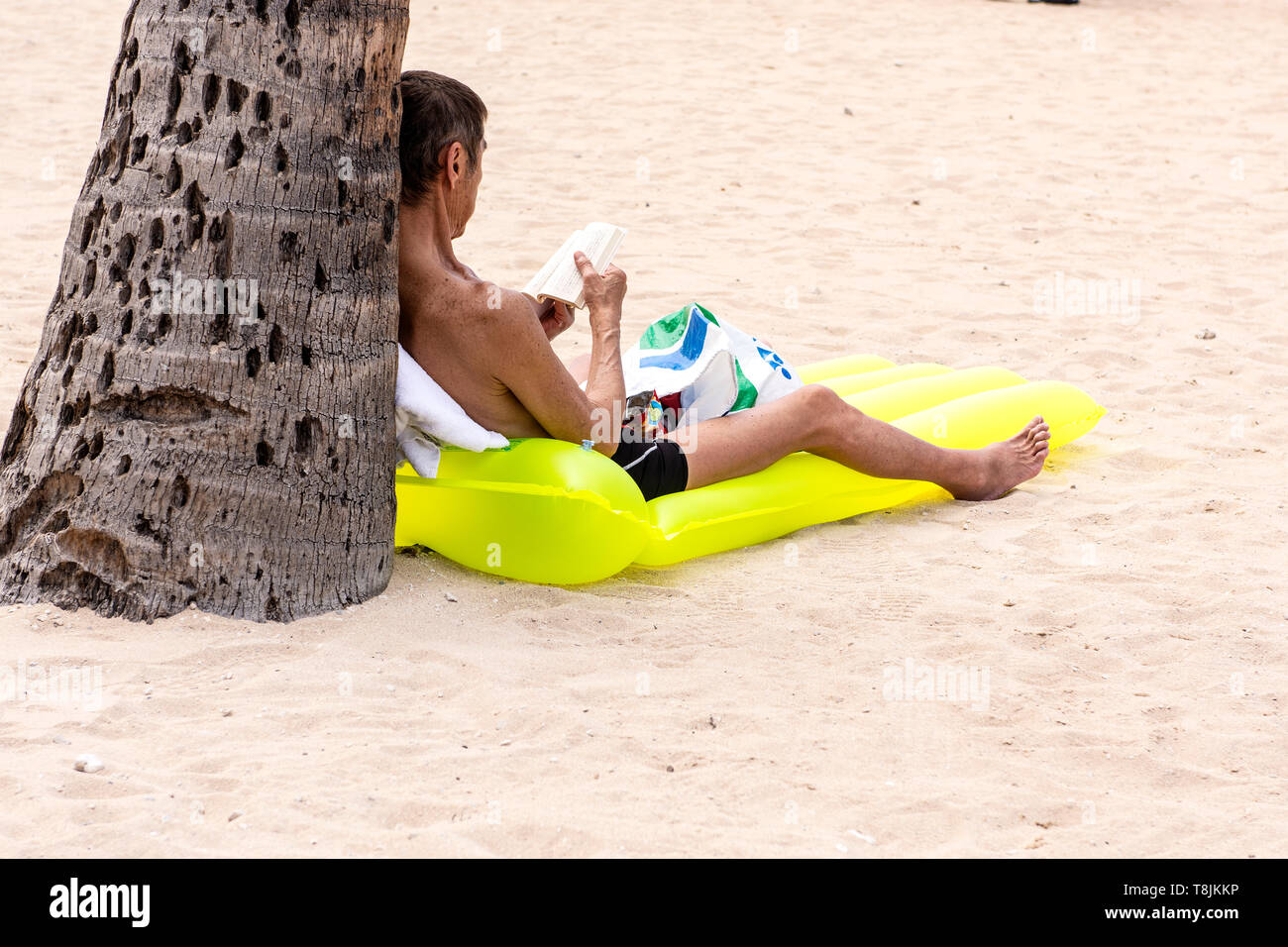 Ein Mann, der alleine sitzt und ein Buch auf einem gelben Schwimmgerät liest, Waikiki Beach, Hawaii, USA. Stockfoto