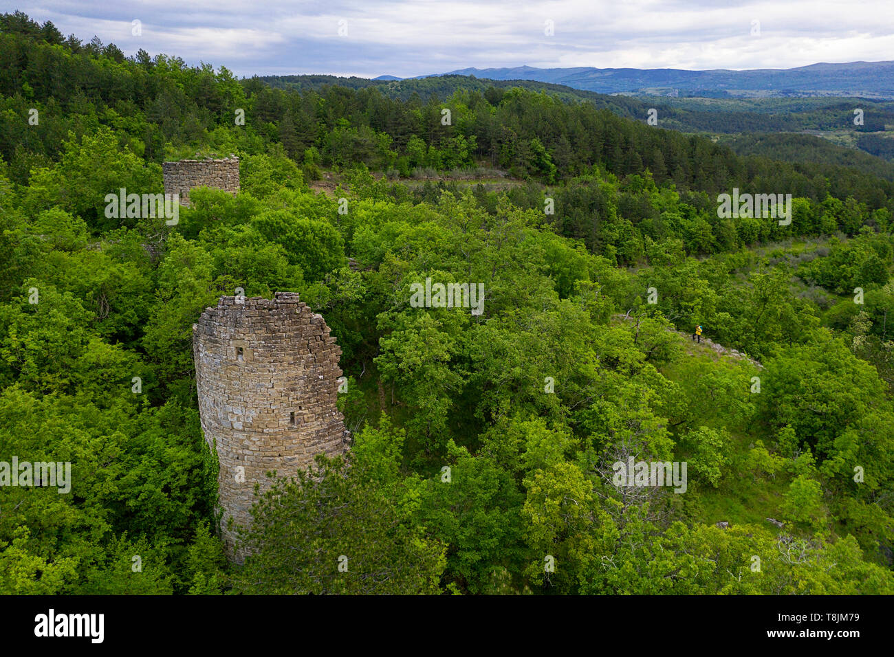 Luftaufnahme der Ruinen von historischen Verteidigung Steinturm und Frau in gelber Jacke im dichten grünen Wald von drohne getroffen. Gradin, Slowenien Stockfoto