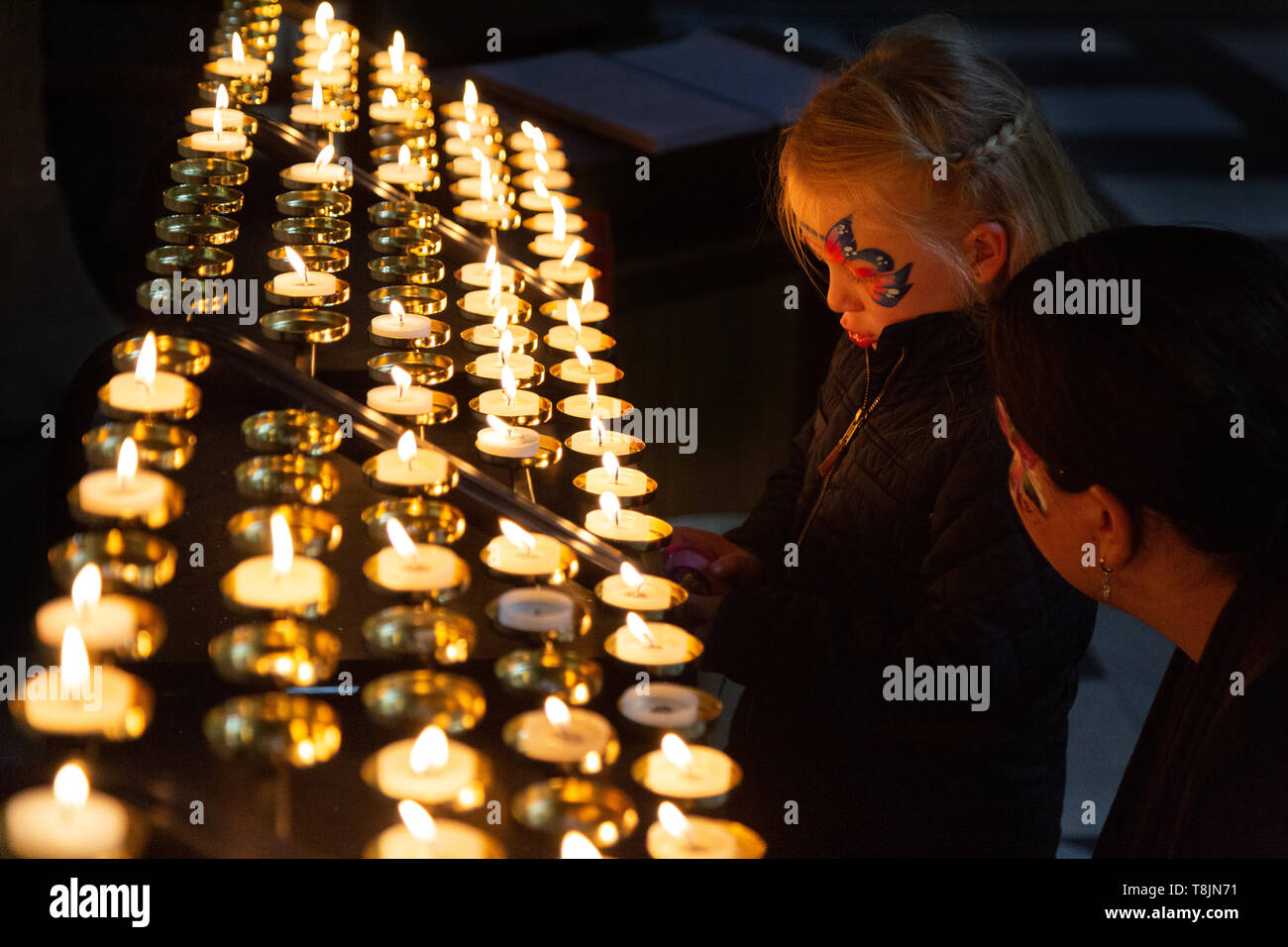 Kind eine Kerze in der Kirche - ein junges Mädchen mit Gesicht Farbe von ihrer Mutter geholfen, eine Kerze anzuzünden; Worcester Cathedral, Worcester, Großbritannien Stockfoto