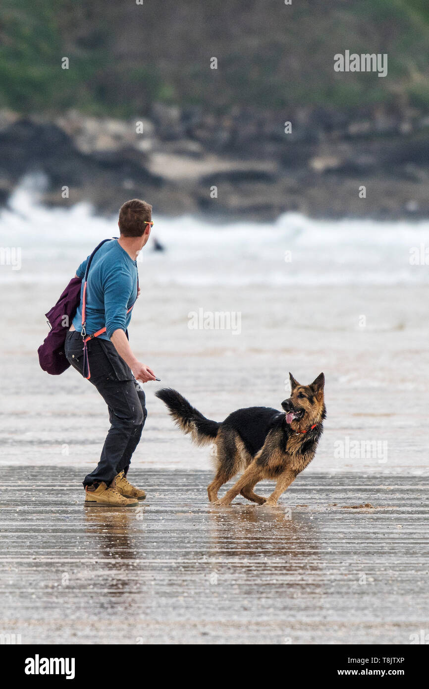Ein Hundebesitzer werfen einen Stein für sein Haustier German Sheperd Hund auf den Fistral Beach in Newquay in Cornwall. Stockfoto