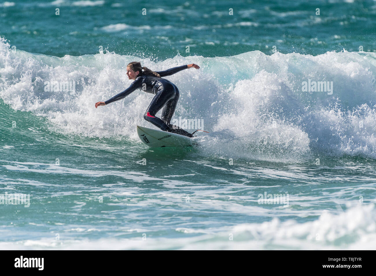 Surfen Aktion als junge Teenager weibliche Surfer reitet eine Welle an Fistral in Newquay in Cornwall. Stockfoto