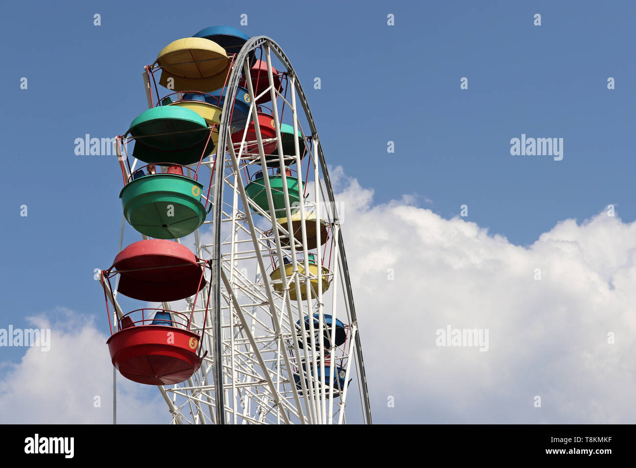 Riesenrad mit bunten Kabinen gegen den blauen Himmel und weißen Wolken. Die Menschen fahren das verdammte Vorderrad im Vergnügungspark Stockfoto