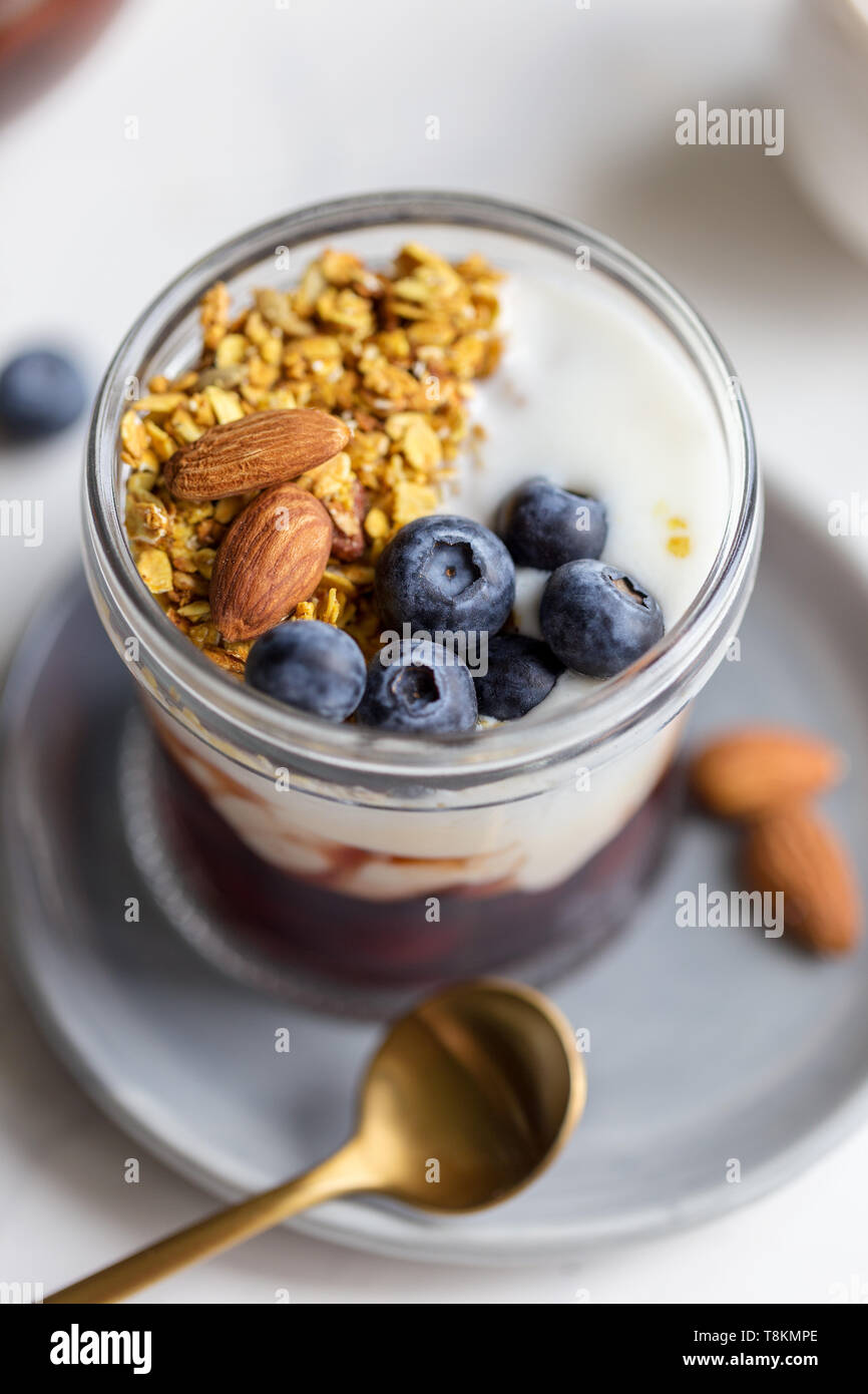 Close up Müsli mit Mandel-, Marmelade, Joghurt und Heidelbeere in Glas, auf der grauen Platte. Konzept der gesunden Frühstück. Hintergrund für Text Stockfoto