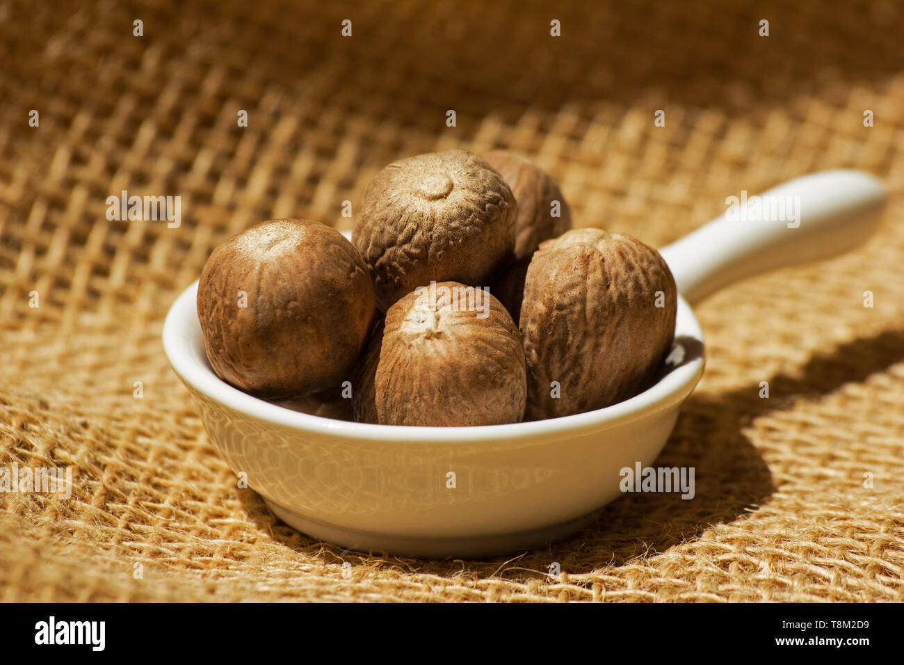 Duftende Muskatnuss in einer weißen Schüssel auf sackleinen Stockfoto