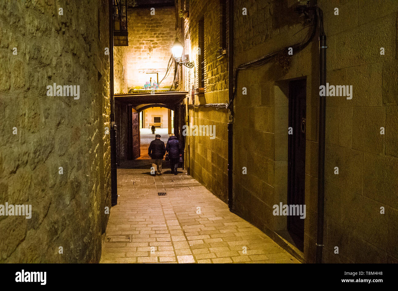Laguardia, Provinz Álava, Baskenland, Spanien: ein Mann und eine Frau laufen unter einem Bogen an einer schmalen Gasse in der Nacht in der historischen Stadt beleuchtet Stockfoto