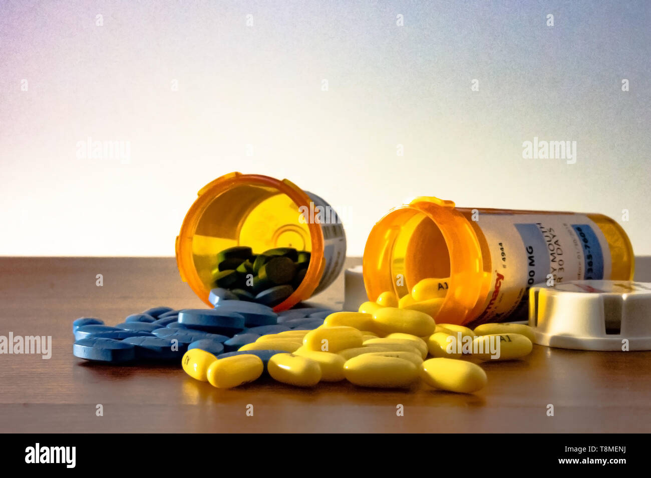 Zwei Verordnungflaschen mit blauen und gelben Pillen Auslaufen auf den Tisch mit einem weißen Hintergrund umgeworfen, was Amerikas Epidemie der p Stockfoto