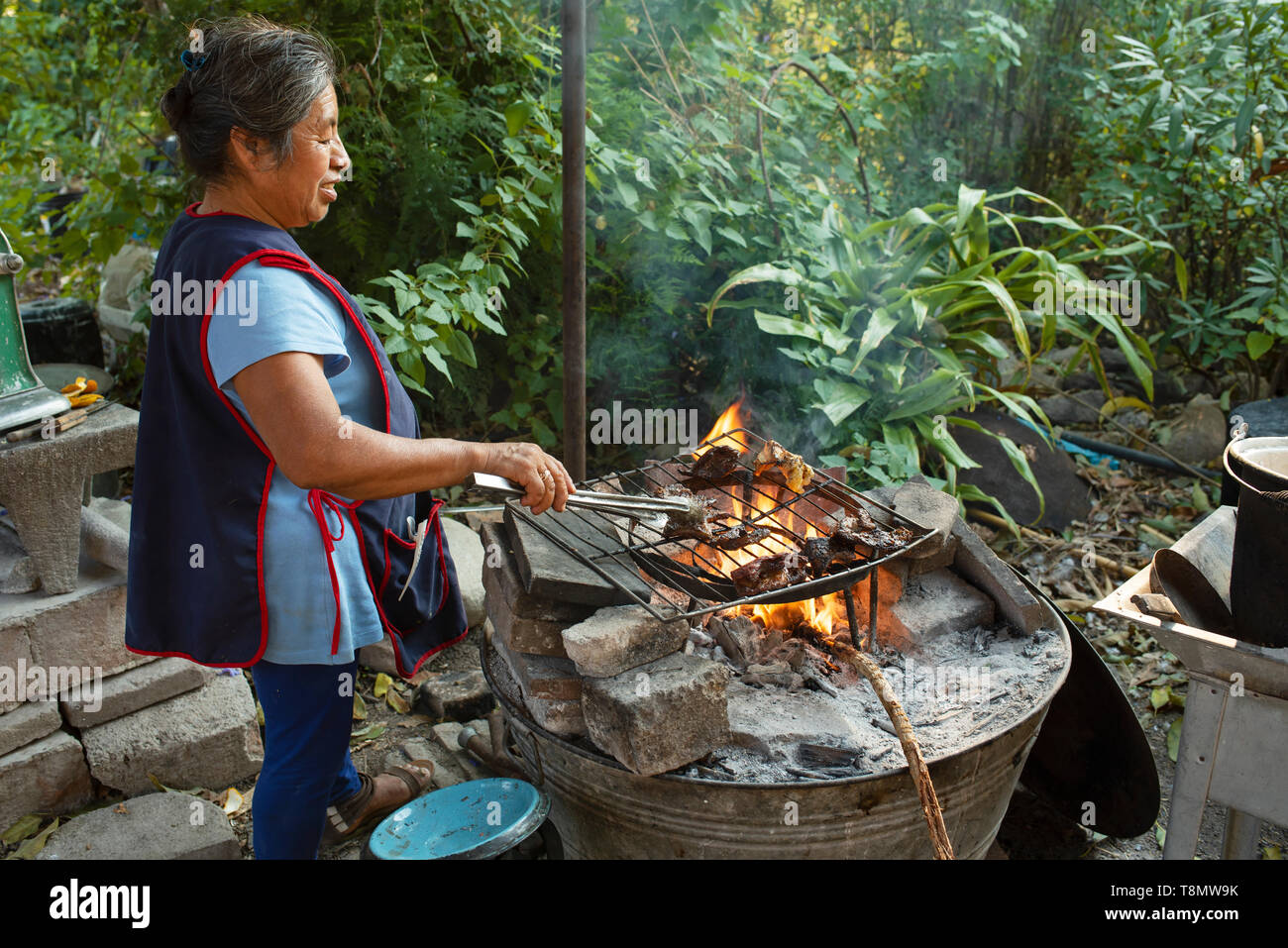 Outdoor Küche mit offenem Kamin. Zapotec Frau braten Fleisch für das Abendessen. Teotitlan del Valle, Oaxaca, Mexiko. Apr 2019 Stockfoto
