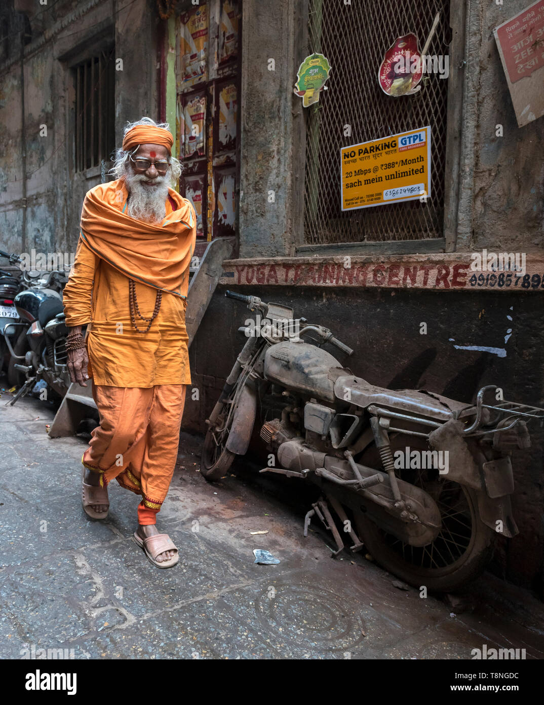 Hindu-priester Spaziergänge Pass eine verlassene Motorrad in den engen Gassen der Altstadt von Varanasi, Indien Stockfoto