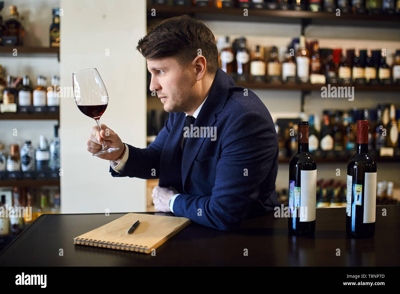Nette junge Mann in modischen blauen Anzug am Tisch sitzen und Verkostung der trinken. Bis schließen Seitenansicht Foto. Stockfoto