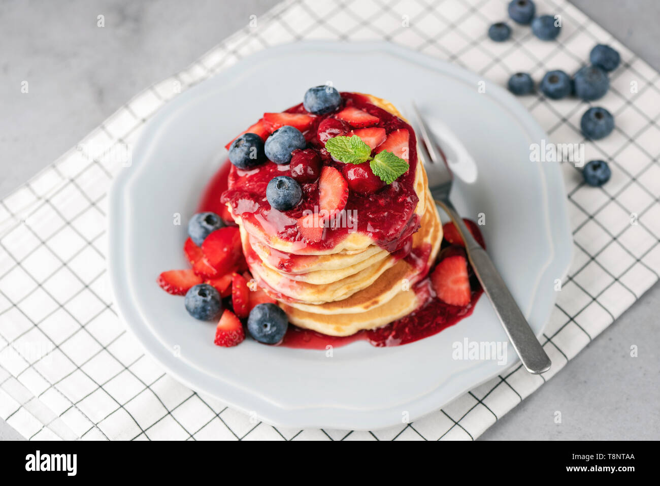 Pfannkuchen mit Beeren und Obst Soße auf der Platte über checkered Tabelle Textil. Gesund leckeres Frühstück Stockfoto