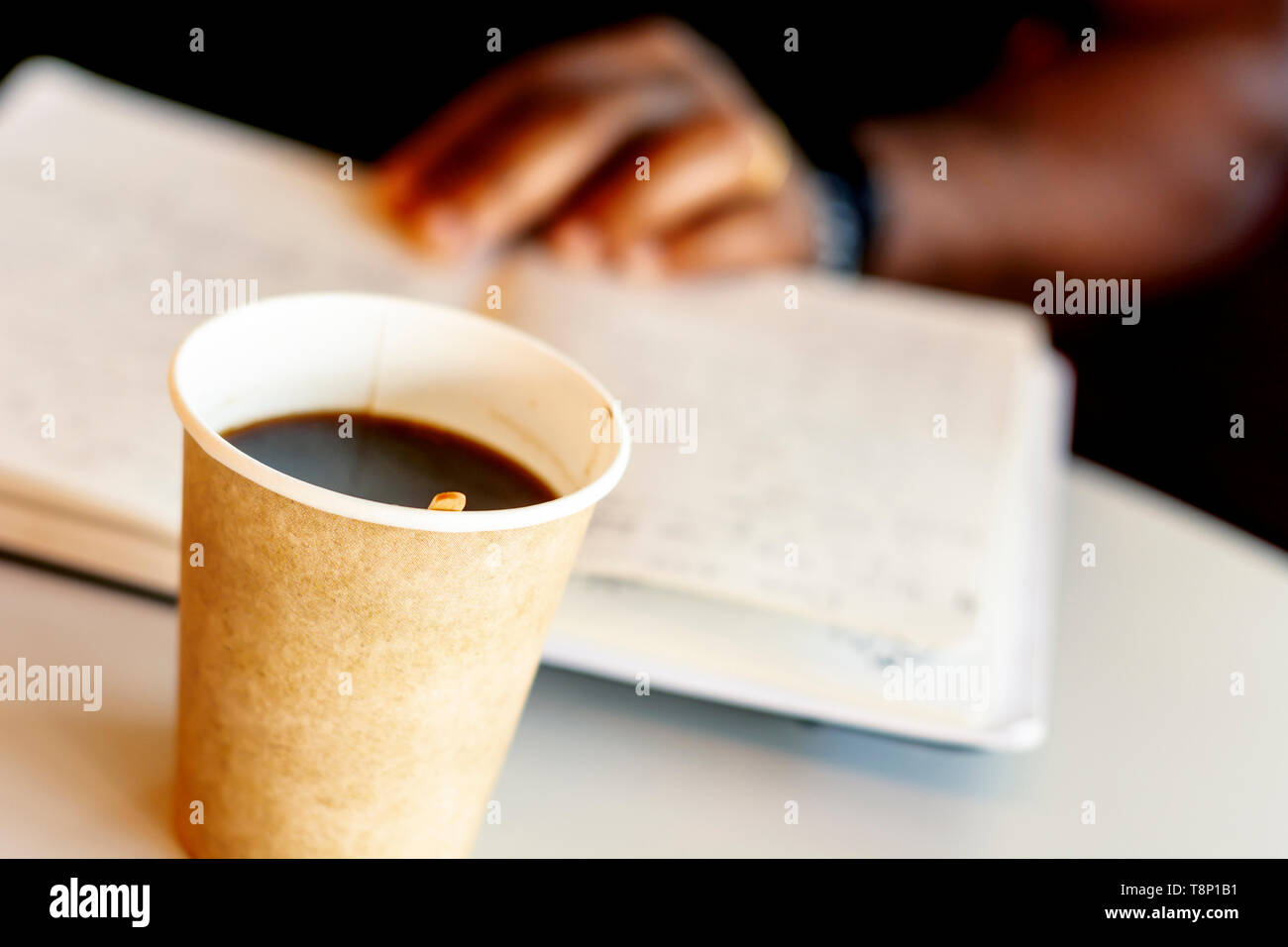 Eine Tasse Kaffee mit einem schwarzen Mann ein Buch lesen im Hintergrund. Eine Pause mit Kaffee Stockfoto