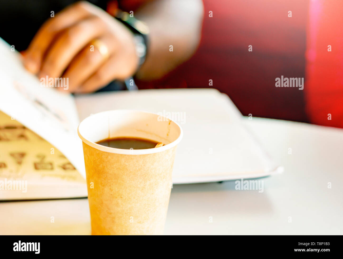 Eine Tasse Kaffee mit einem schwarzen Mann ein Buch lesen im Hintergrund. Eine Pause mit Kaffee Stockfoto