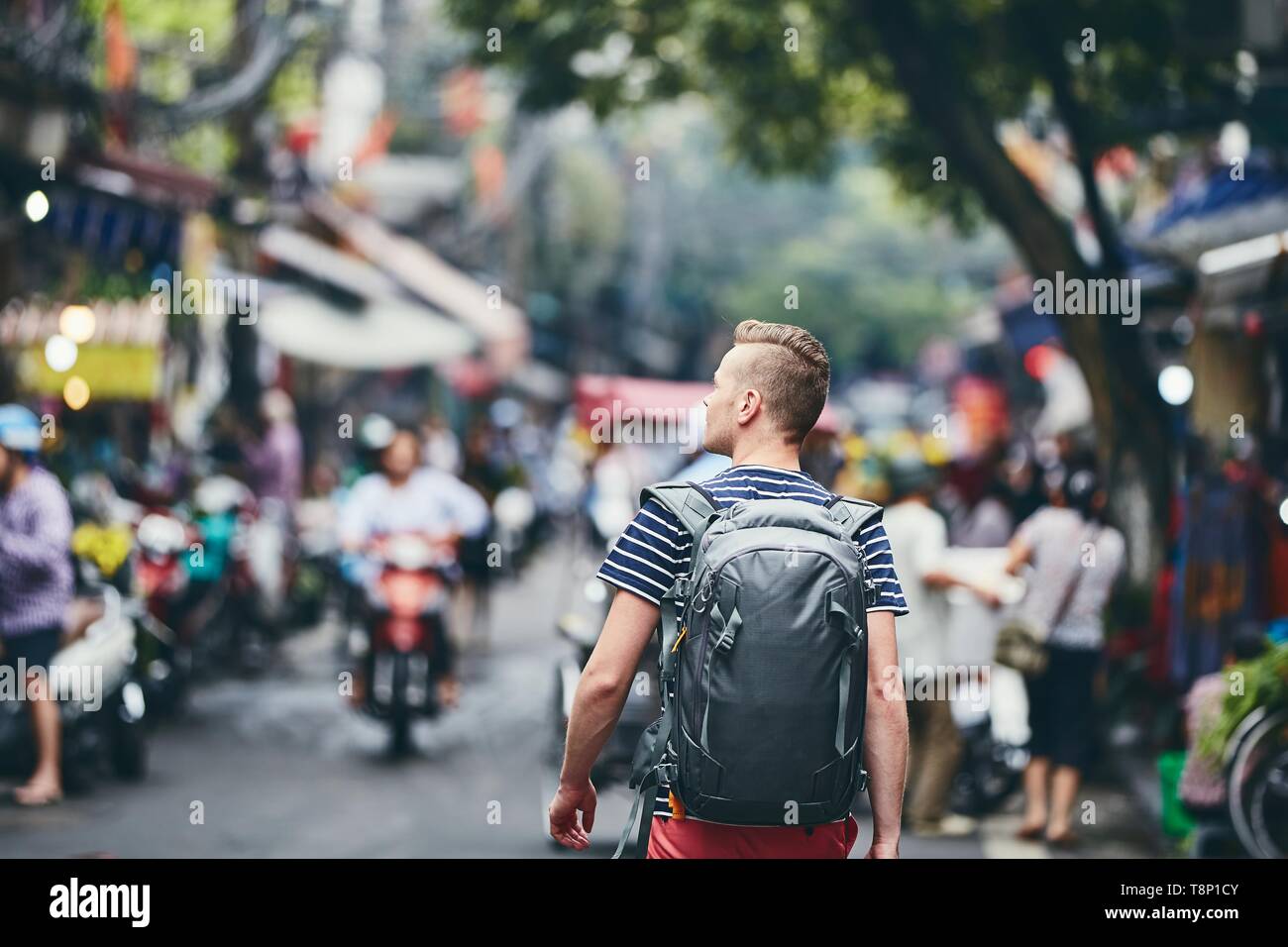 Reisenden zu Fuß auf stark befahrenen Straße. Ansicht der Rückseite des jungen Mann mit Rucksack in Hanoi, Vietnam. Stockfoto