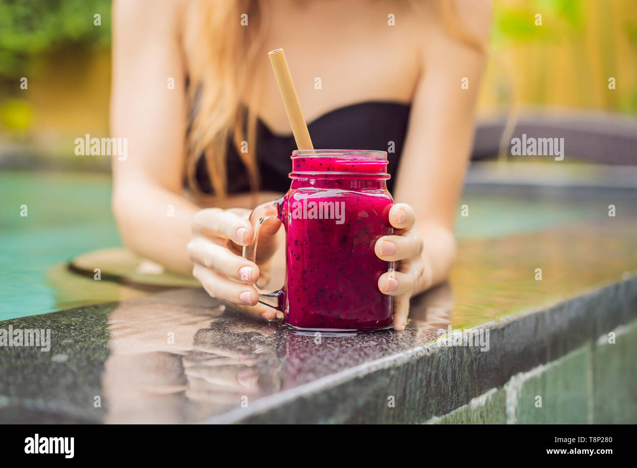 Junge Frau trinkt Dragon Fruit Smoothies auf dem Hintergrund der Pool. Fruit Smoothie - gesunde ernährung Konzept. Nahaufnahme von detox Smoothie mit Stockfoto