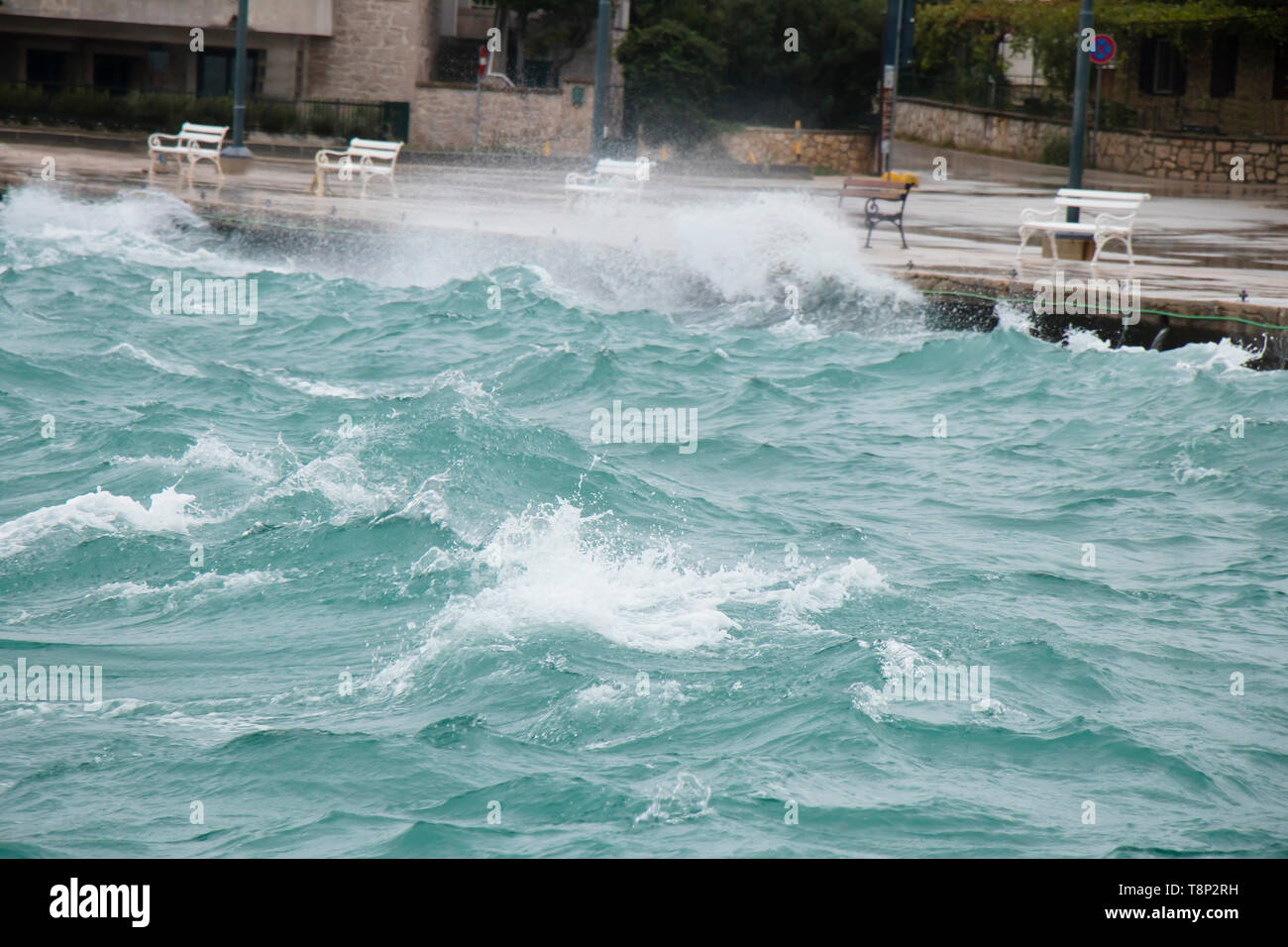 Stürmische See plätschern die Wellen an der Küste Promenade mit Bänken in Dalmatien Stadt am Meer in der Nebensaison bei starkem Südwind mit Regen Stockfoto