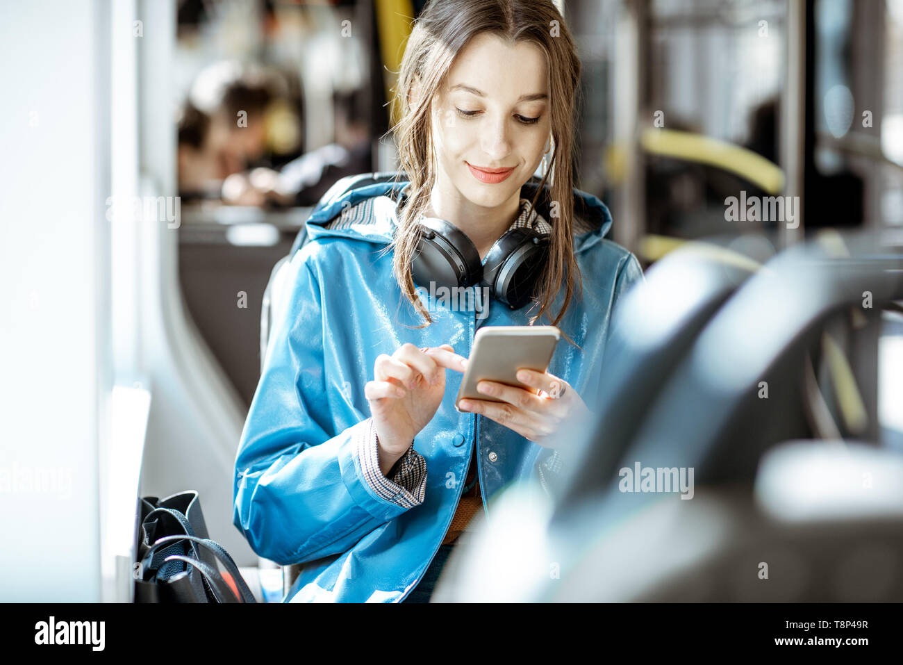 Junge elegante Frau mit öffentlichen Verkehrsmitteln, Sitzung mit Telefon und Kopfhörer in der modernen Straßenbahn Stockfoto