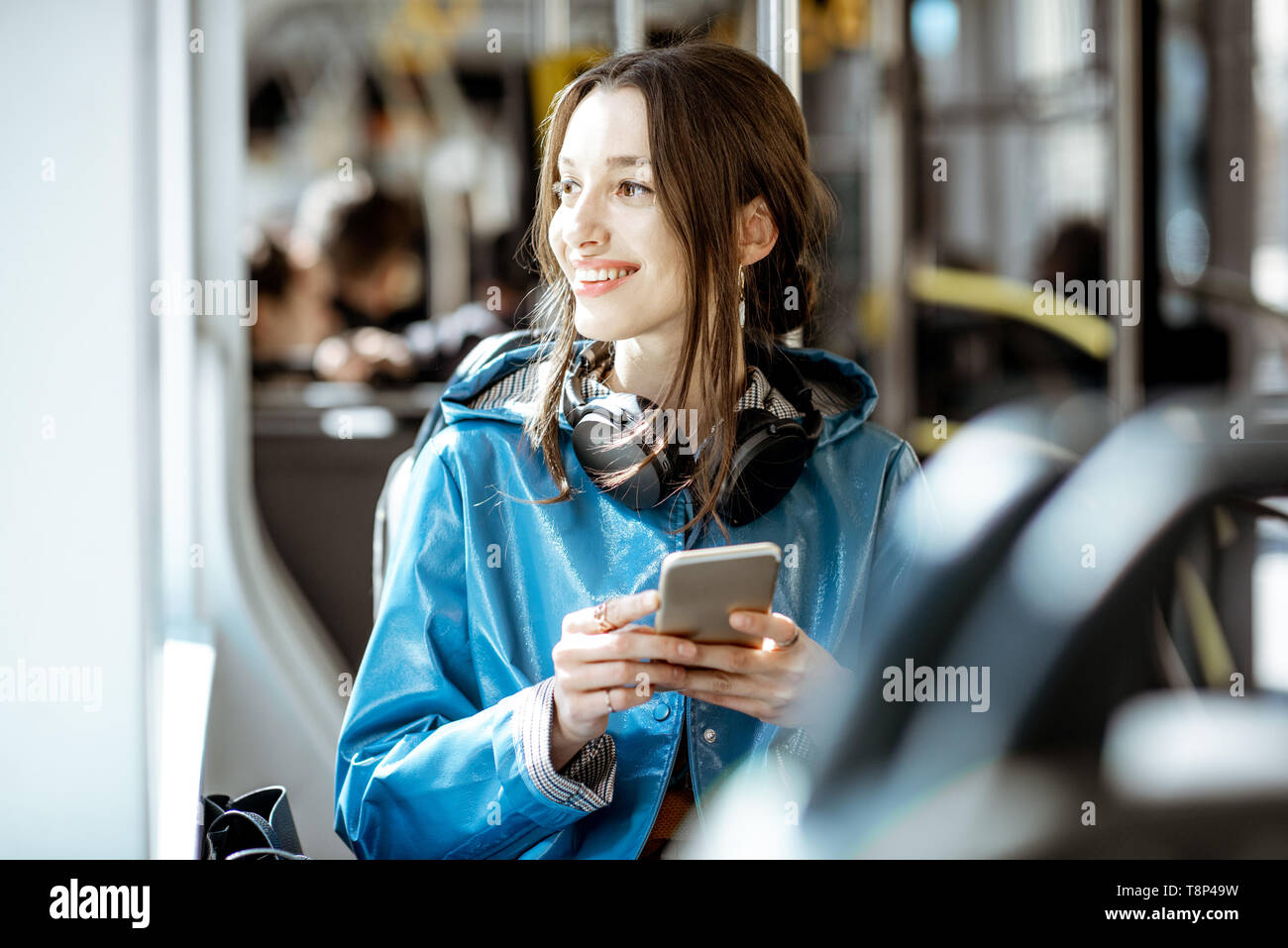 Junge elegante Frau mit öffentlichen Verkehrsmitteln, Sitzung mit Telefon und Kopfhörer in der modernen Straßenbahn Stockfoto