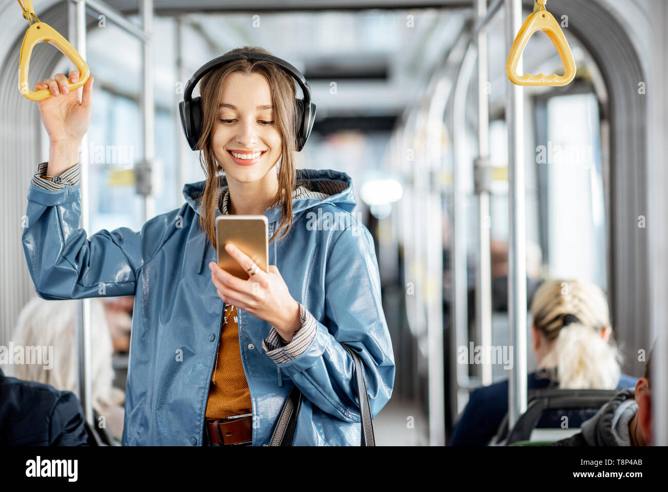 Junge Frau Passagier stehend mit Kopfhörern und Smartphone, während in der modernen Straßenbahn Bewegen, geniessen Urlaub im öffentlichen Verkehr Stockfoto