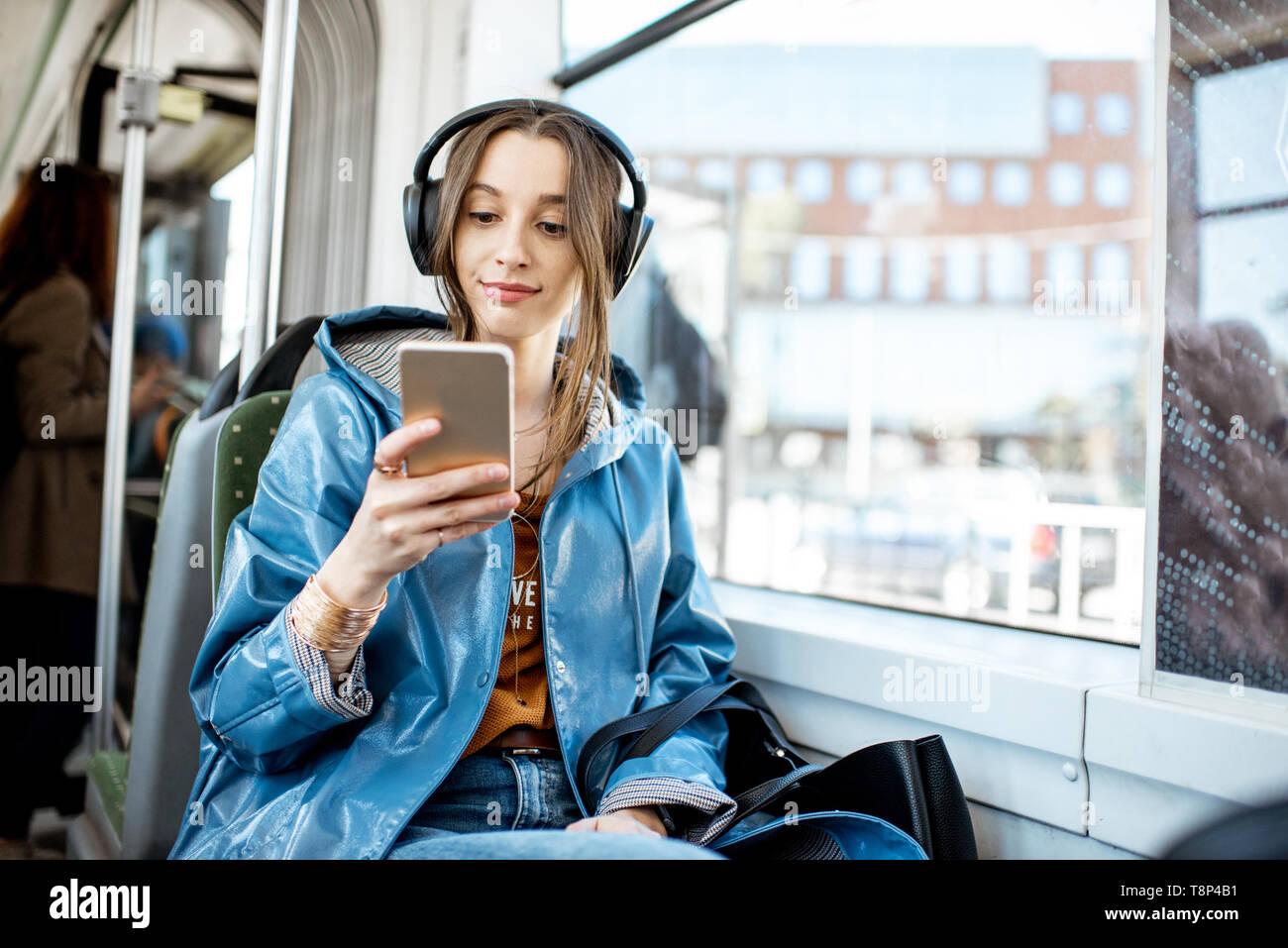 Junge Frau Passagier genießen Urlaub im öffentlichen Verkehr, sitzend mit Kopfhörern in der Nähe der Fenster in der modernen Straßenbahn Stockfoto