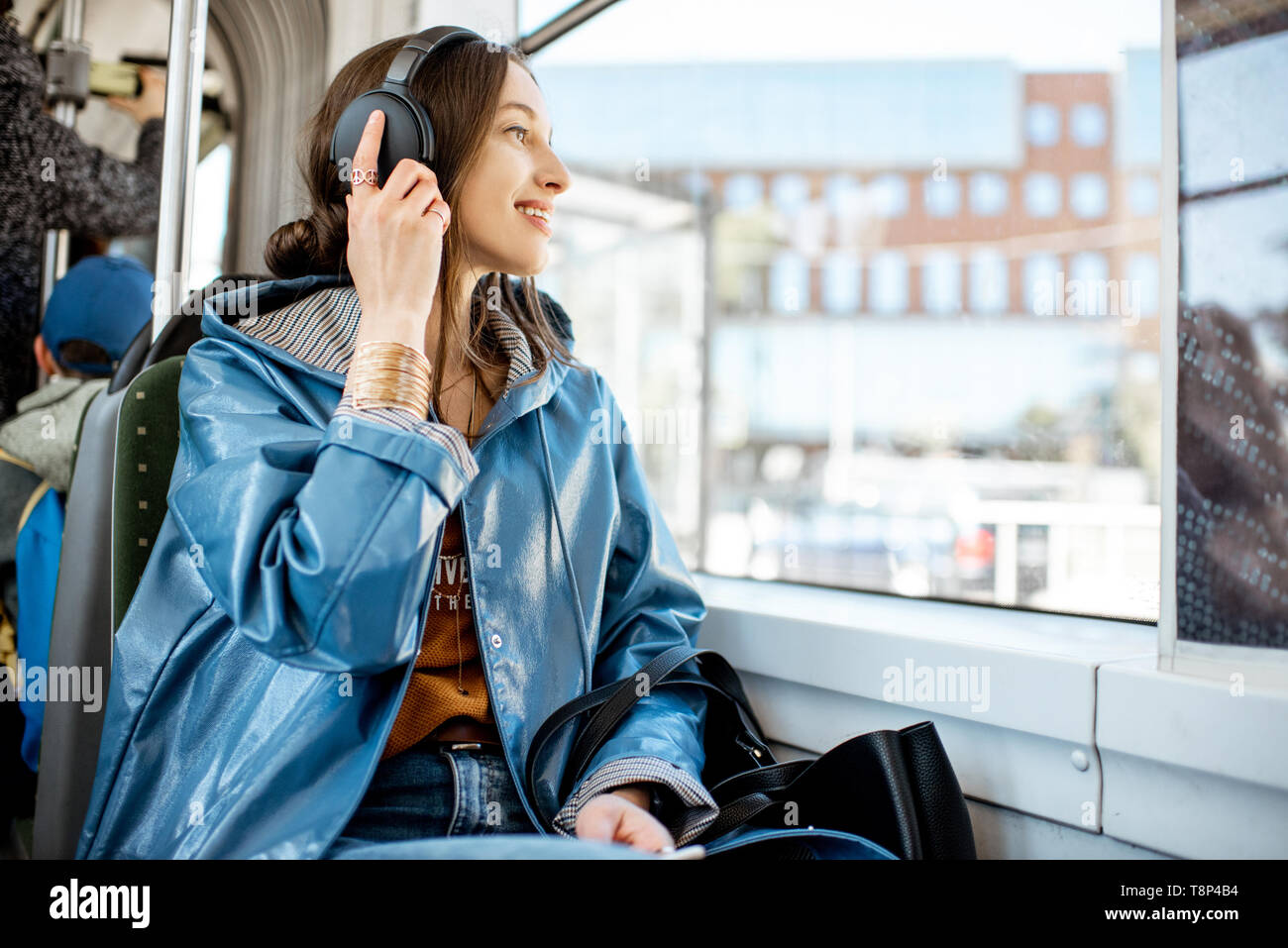 Junge Frau Passagier genießen Urlaub im öffentlichen Verkehr, sitzend mit Kopfhörern in der Nähe der Fenster in der modernen Straßenbahn Stockfoto