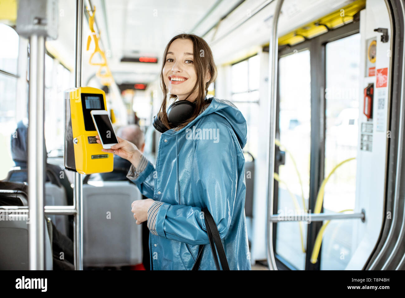 Portarit eines junge lächelnde Frau Zahlung conctactless mit Smartphone für die öffentlichen Verkehrsmittel in der Straßenbahn Stockfoto