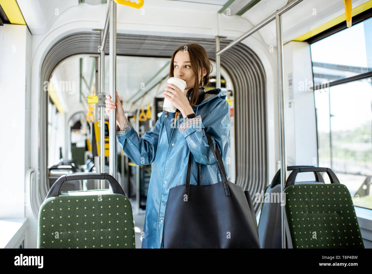 Junge stilvolle Frau genießen Reise in der modernen Straßenbahn, stehend mit Kaffee in den öffentlichen Verkehrsmitteln Stockfoto