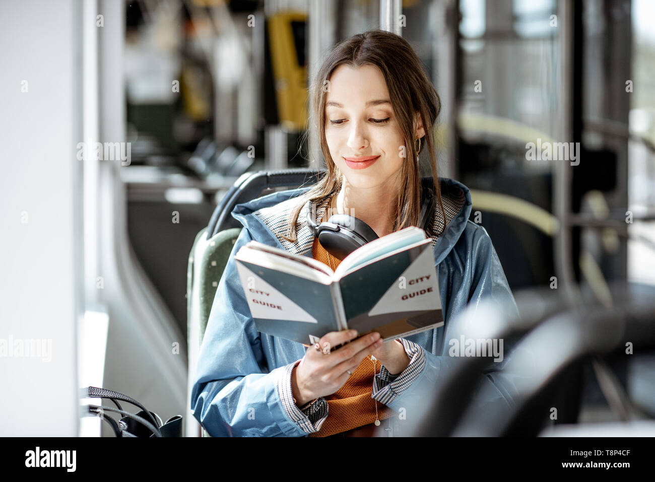 Junge Frau mit Buch beim Bewegen in der modernen Straßenbahn, glücklich Passagier an der öffentlichen Verkehrsmittel Stockfoto