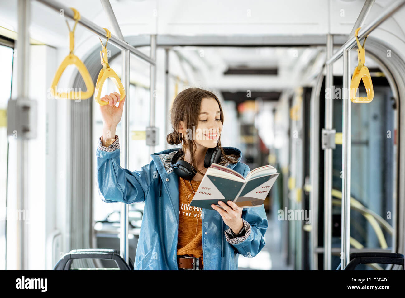 Junge Frau mit Buch, während in der modernen Straßenbahn stehend, glücklich Beifahrerseite Verschieben von bequemen öffentlichen Verkehrsmitteln Stockfoto