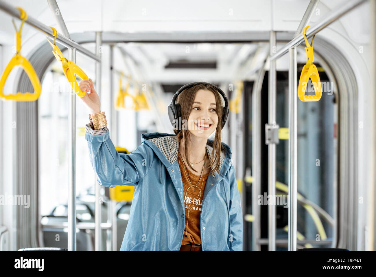 Junge Frau mit Griff während der Fahrt in modernen Straßenbahn. Glückliche Passagiere genießen Urlaub im öffentlichen Verkehr Stockfoto
