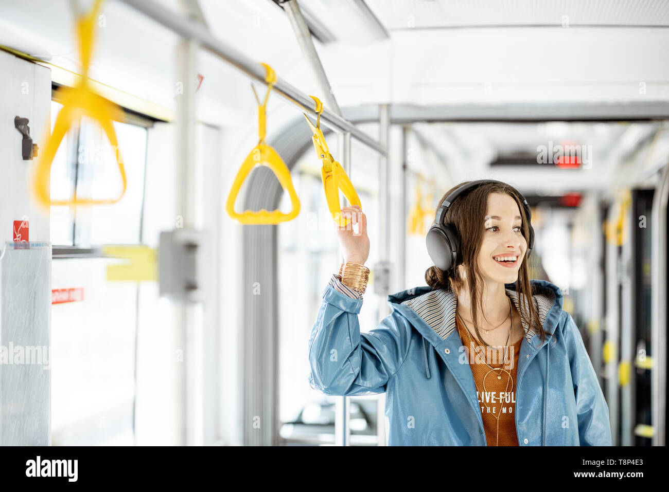 Junge Frau mit Griff während der Fahrt in modernen Straßenbahn. Glückliche Passagiere genießen Urlaub im öffentlichen Verkehr Stockfoto