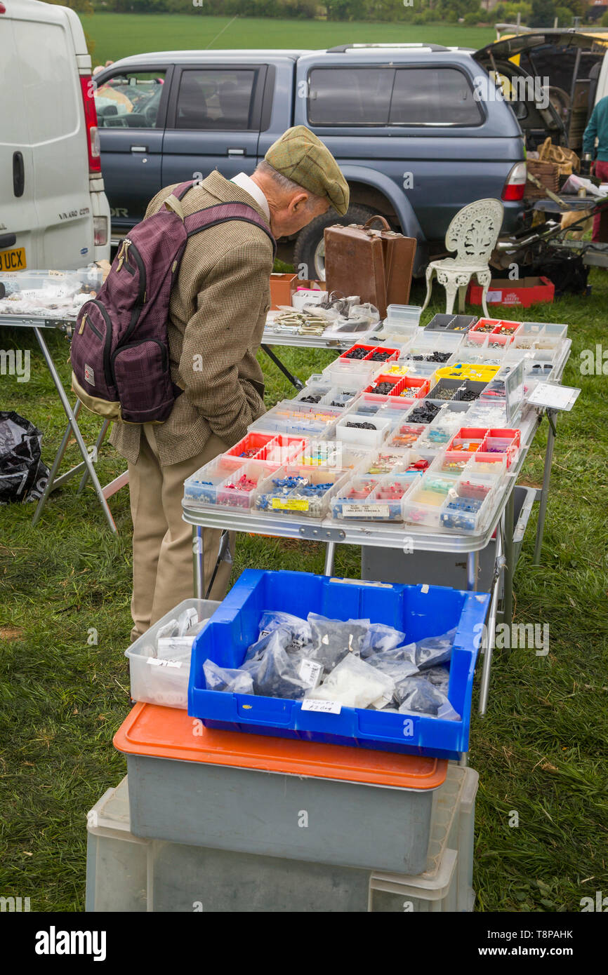 Ein älterer Mann mit einem Tweed Jacke und flacher Deckel prüft Auto Teile an einem teilemarkt auf ein Land zeigen. Stockfoto Ein älterer Mann mit einem Tweed Jacke und flacher Deckel prüft Auto Teile an einem teilemarkt auf ein Land zeigen. Stockfoto