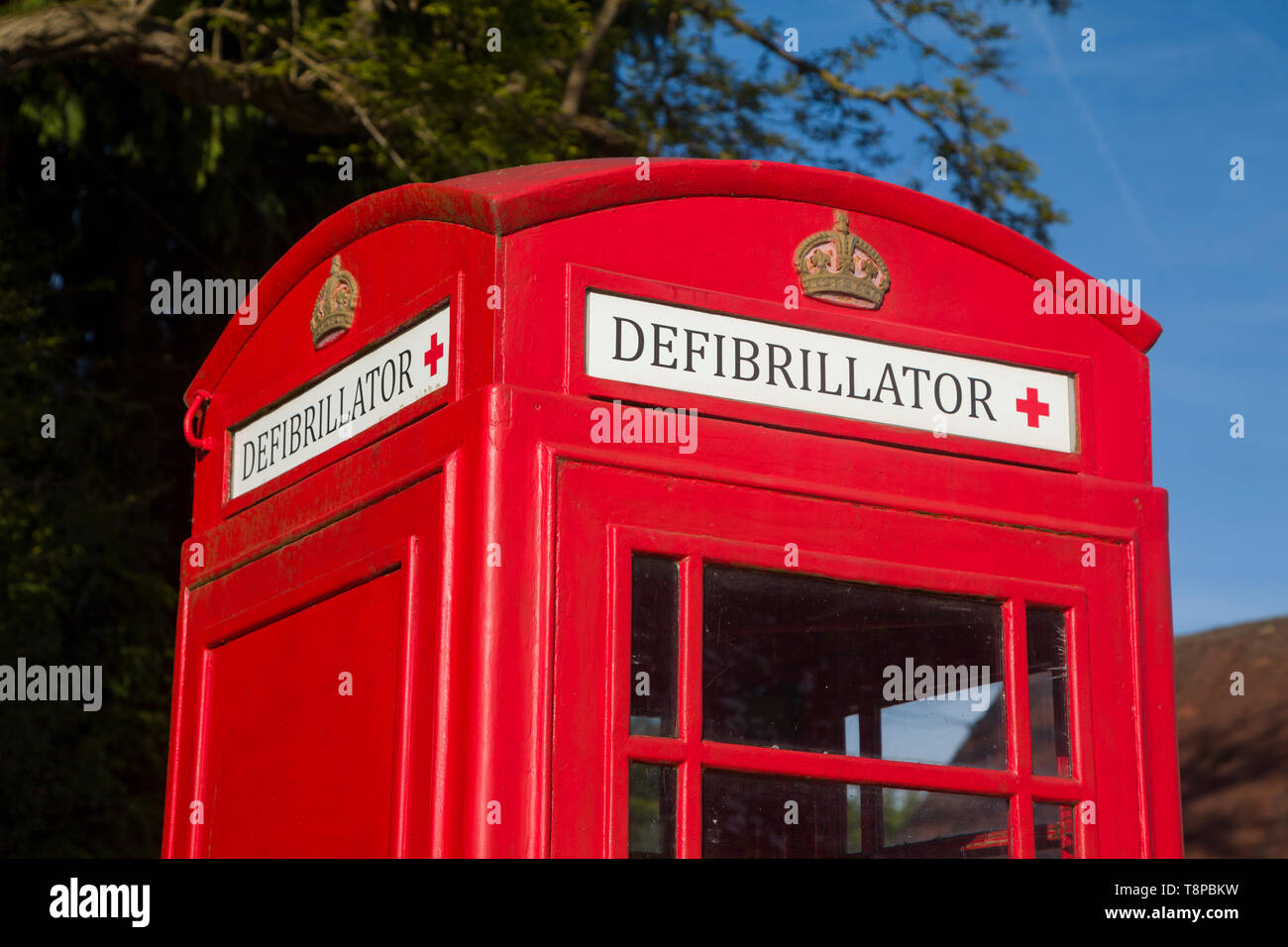 Eine leuchtend rote, traditionelle öffentliche Telefonbox, die in Peppard Common, Oxfordshire, zum Haus eines Notfall-Defibrillators in der Gemeinde umgebaut wurde Stockfoto