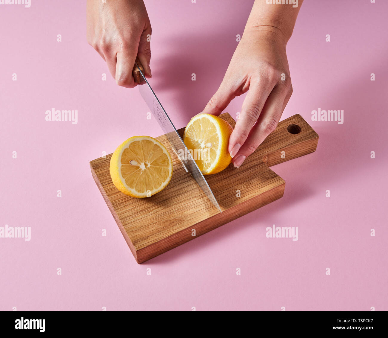 Die Frau Hände schneiden Sie eine Zitrone auf einem Holzbrett mit Messer um ein rosa Hintergrund mit kopieren. Zutat für den Sommer trinken Stockfoto