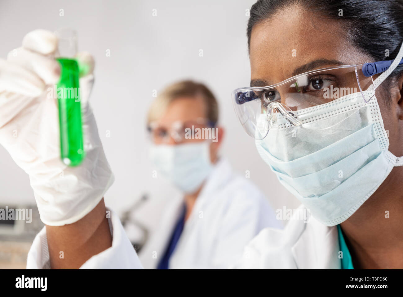 Asiatische Frau Frau medizinische oder wissenschaftliche Forscher oder Arzt an einem Test Tube grüne Lösung in einem Labor oder Labor mit ihrem Kollegen suchen Stockfoto