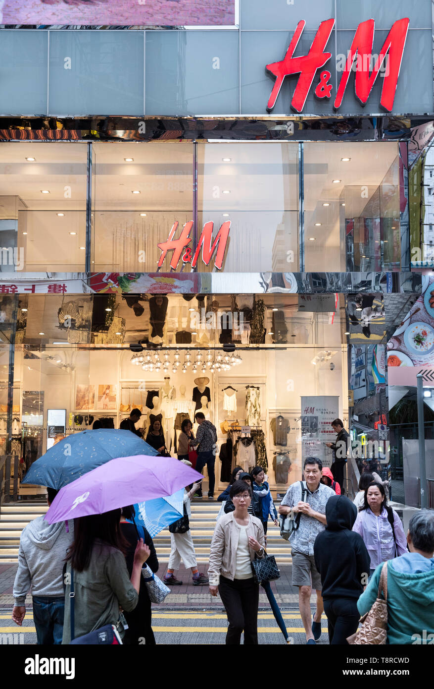 Fußgänger gesehen Überqueren der Straße vor einem schwedischen multinationalen Kleidung Design retail Unternehmen Hennes & Mauritz, H&M, Store in Hongkong. Stockfoto