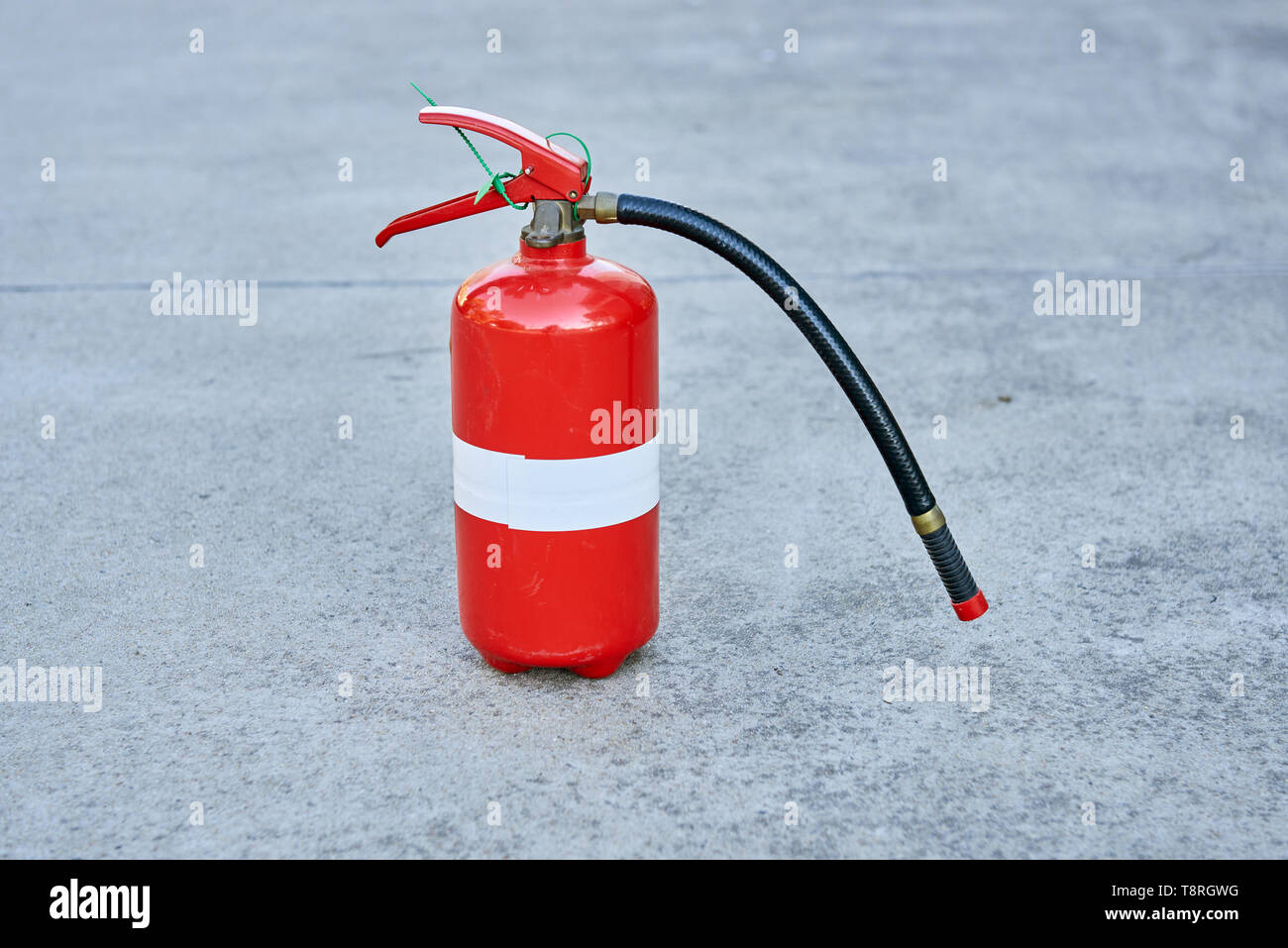 Ein einzelnes isoliertes Feuerlöscher auf Beton in Rot mit weißem Streifen Klebeband um die Mitte. Stockfoto